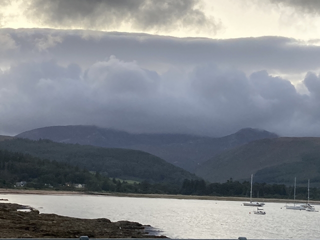Mountains shrouded in clouds with water in the foreground.