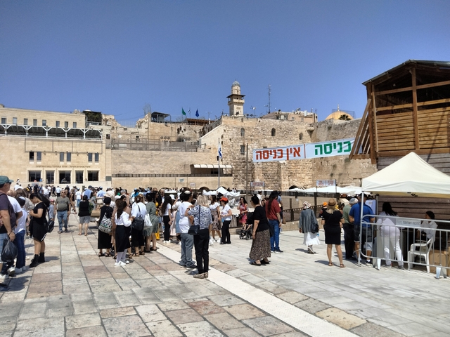       Large open plaza with people, banners, and historic walls.
  