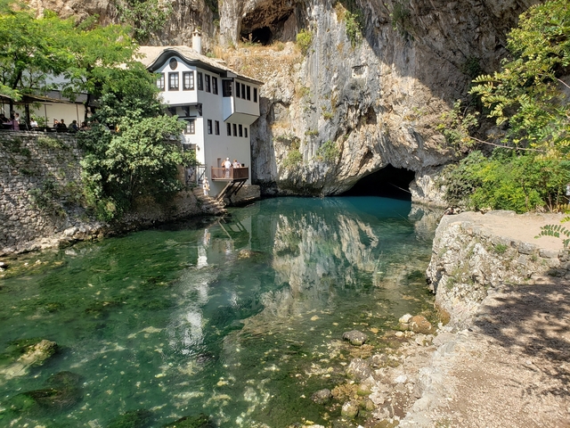 Small group of people at the entrance of a cave by a river.