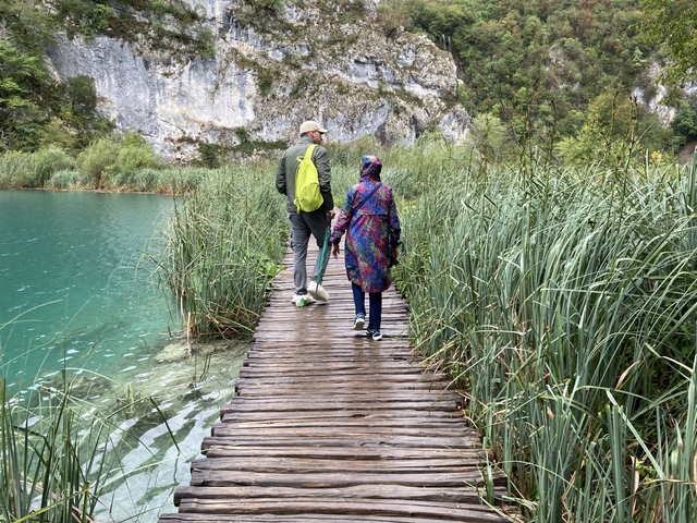 A couple walking on a wooden boardwalk over a green lake.