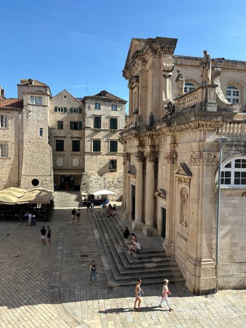 Historic building with stairs and people on a cobblestone street.