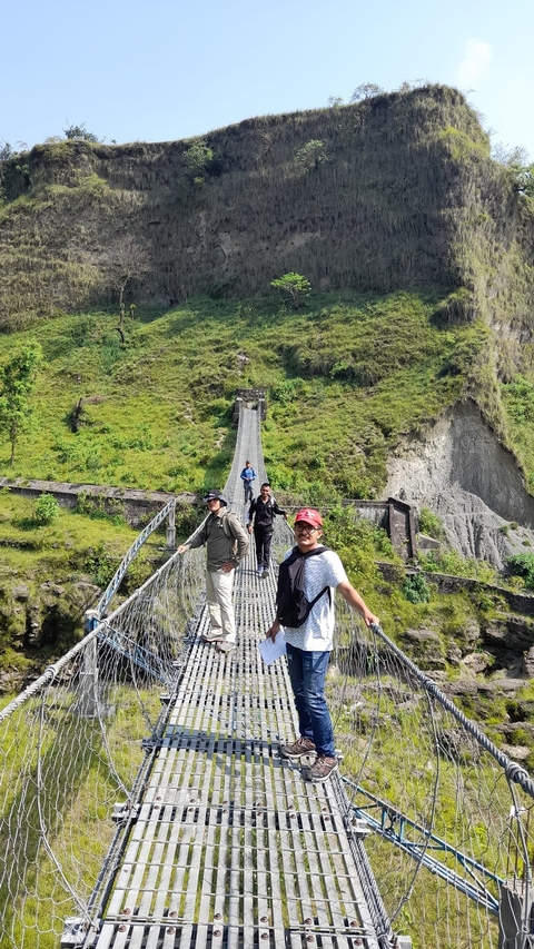       Hikers crossing a suspension bridge in a mountain area.
  