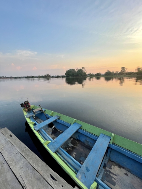       A wooden boat on a calm river at sunset with trees lining the banks.
  
