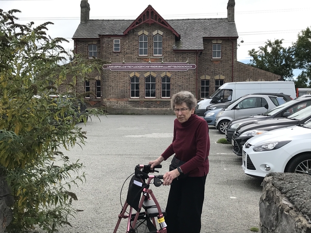Person with a walker in a parking area with a long, unique building in the background.