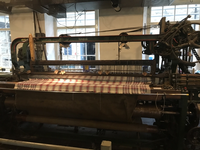 Indoor scene of a weaving machine with a cloth in progress.