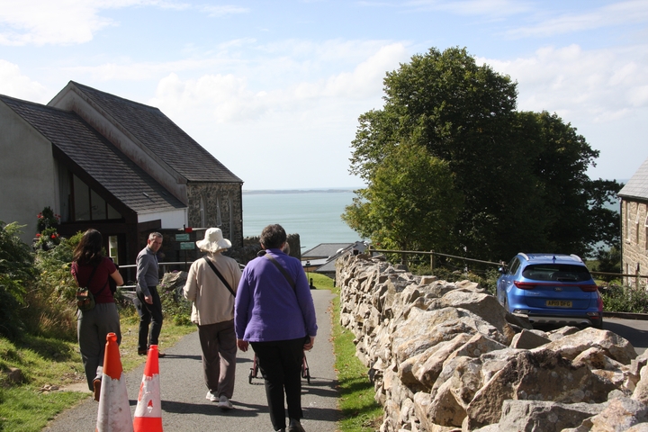       Group of people walking towards the sea on a path lined with stone walls.
  