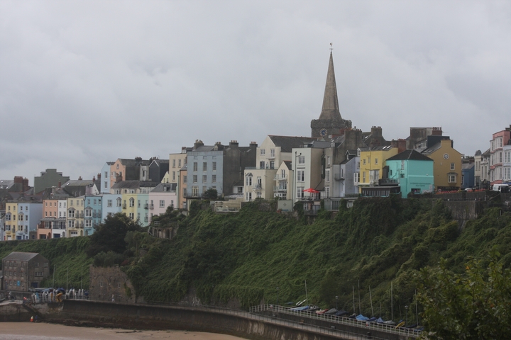 Colorful houses on a hill with a church tower above lush greenery.
