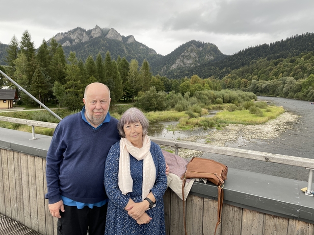 Couple posing on a bridge with mountain landscape and river.
