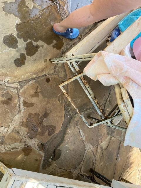       Wet floor with a folded rusty chair and a foot in sight.
  