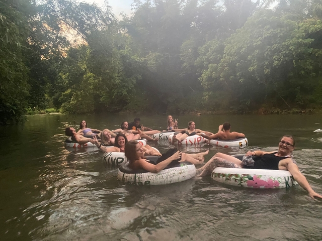       People lounging on inflatable rings in a river surrounded by greenery.
  