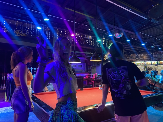       People playing pool in an indoor venue with colorful lights.
  