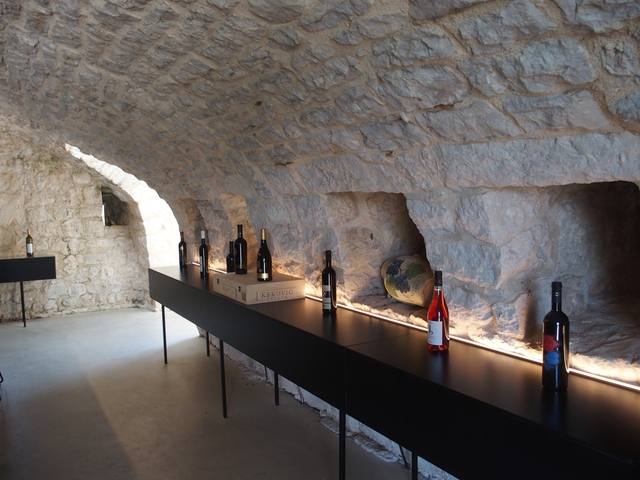 Interior with light stone walls and wine bottles on display.