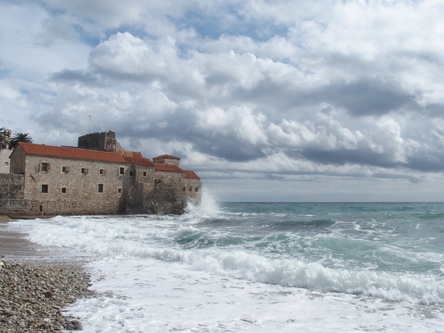       Waves crashing against a historic stone building by the sea.
  
