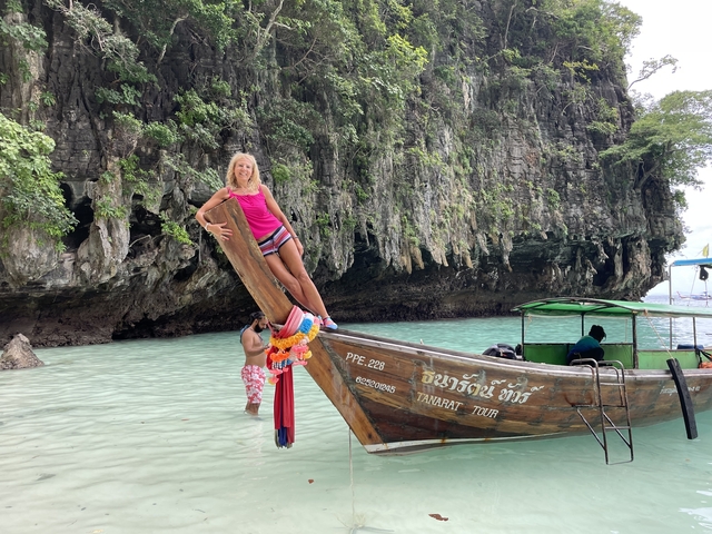 Person posing on a traditional boat with a rocky coastline.