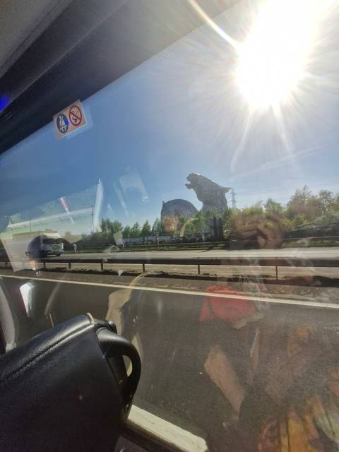       View from a vehicle window showing a road and distant structures.
  