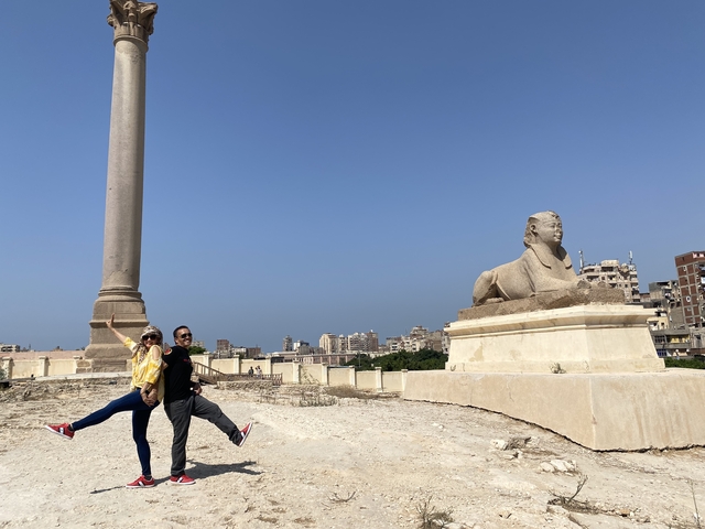 Couple posing near an ancient sphinx and column.