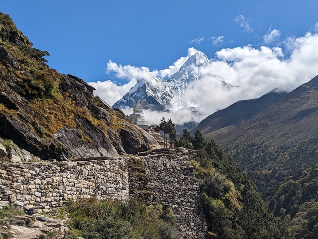 Mountain landscape with a stupa and a walking path, partially obscured by clouds.