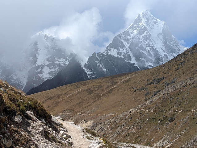 Mountainous terrain with a hiking path, clouds partially covering the peaks.