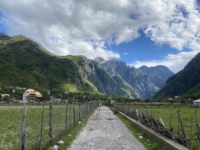 Mountain valley view with a path leading towards the mountains and houses along the way.