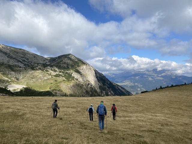 Hikers walking through a valley with mountains and clouds.