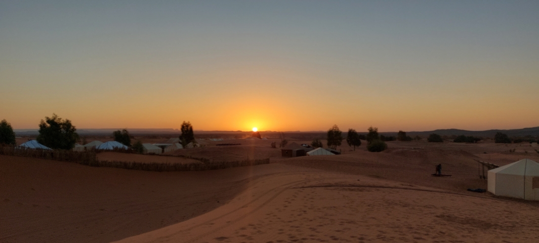       Sunset over a desert with scattered tents.
  