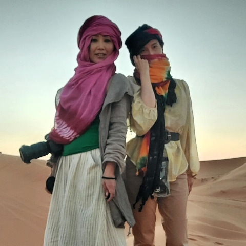       Two people standing in a desert with scarves covering their faces.
  
