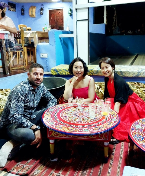       Three people sitting at a colorful table in a Moroccan setting.
  