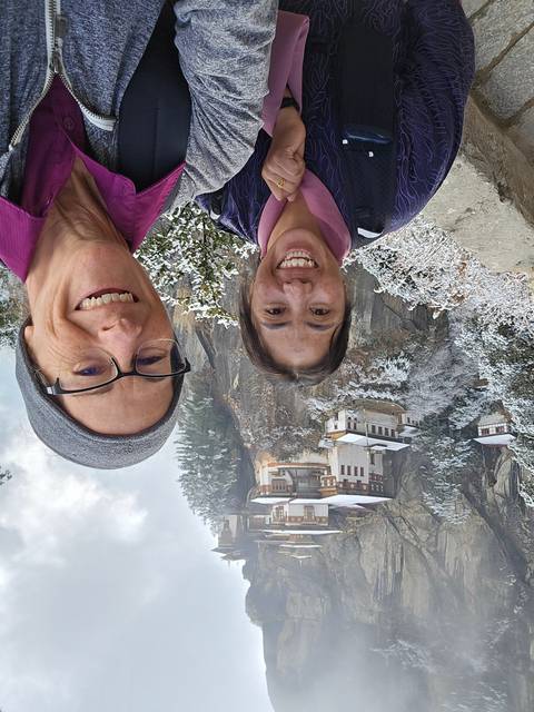 Two people smiling in front of Paro Taktsang monastery.