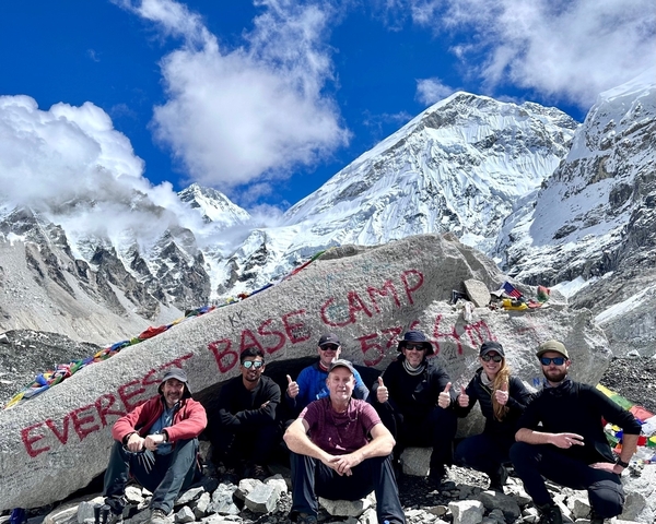 Group of people posing at Everest Base Camp with snowy peaks.