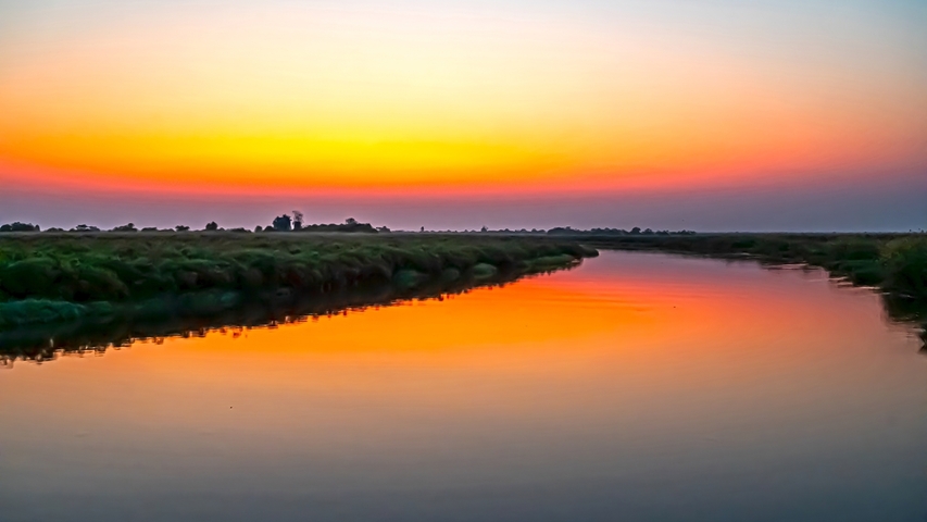       Colorful sunset over a calm river with lush banks.
  