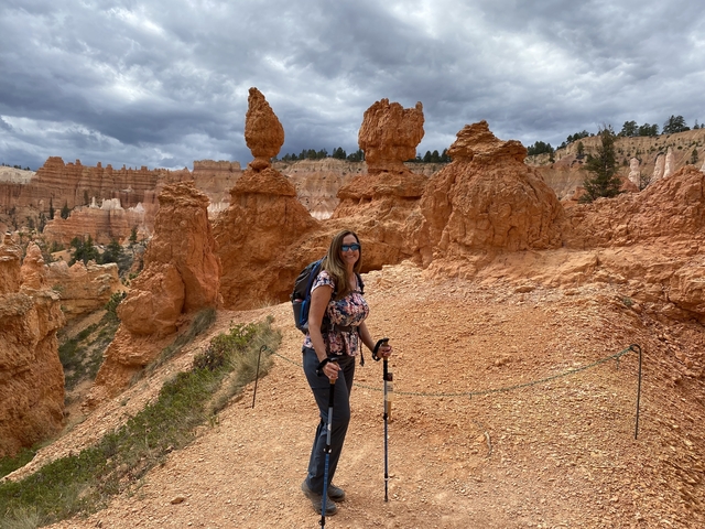       Hiker amongst orange hoodoos in a canyon landscape.
  