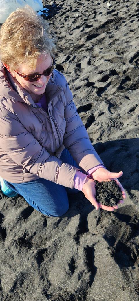       Person holding black sand on a beach.
  