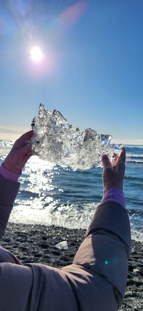       Person holding a piece of ice with the ocean in the background.
  