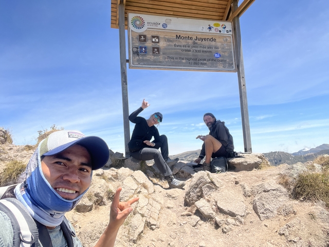       Three people posing with a sign indicating a summit.
  