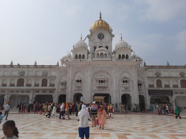       Sikh temple with white and gold domes, surrounded by visitors.
  