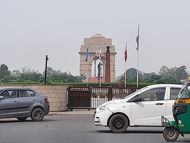       India Gate monument with flags and parked vehicles in the foreground.
  