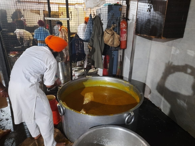       Person stirring large pot of food in a stainless steel kitchen.
  