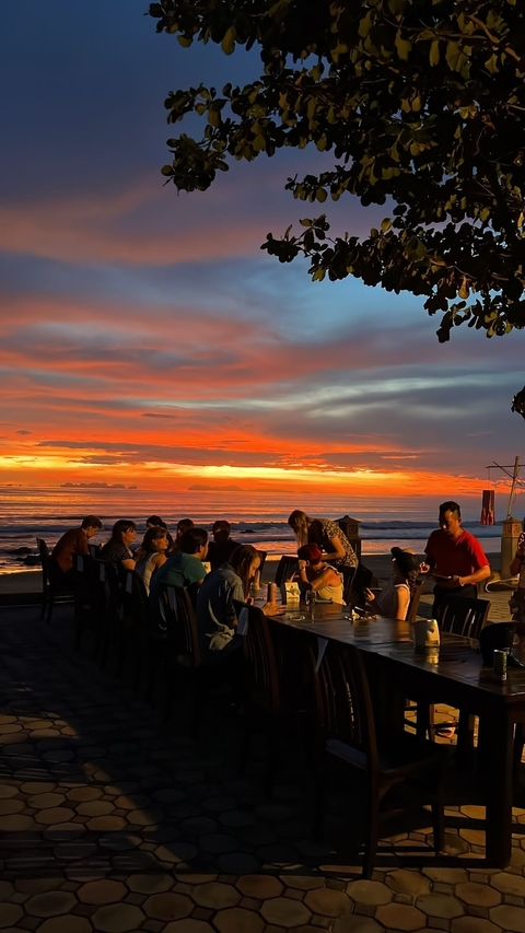 Group of people dining at a beachside restaurant during sunset.