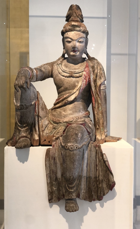 Weathered stone statue of a seated figure in a museum.