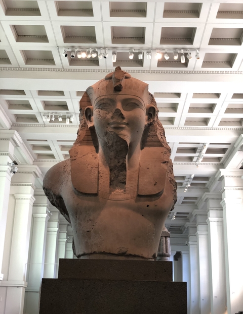 Bust of a sphinx in a museum with a damaged face.