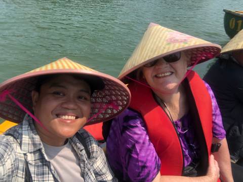       Smiling people in traditional conical hats on a boat.
  
