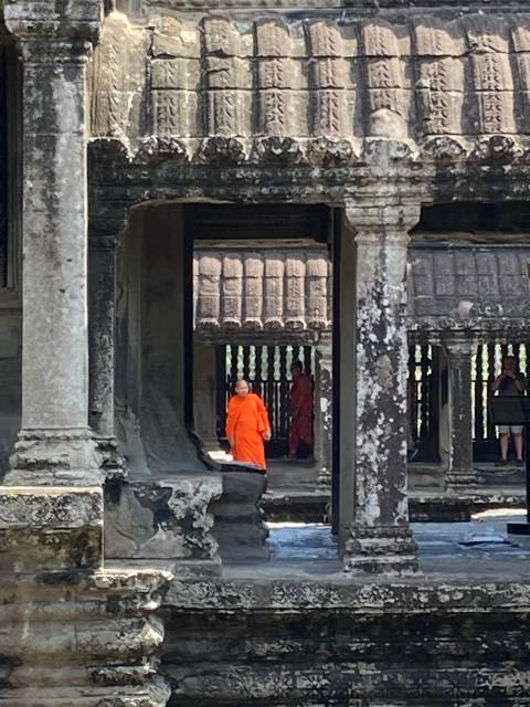       Person in orange robe inside a temple with intricate stone architecture.
  