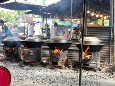 Outdoor street food market with large pots on stove.