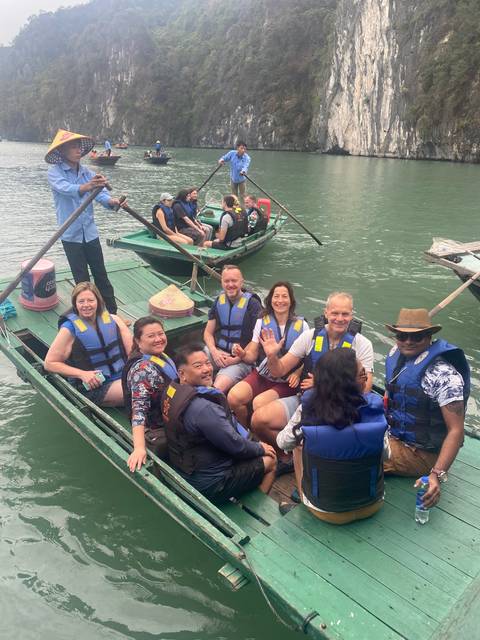       Group of people in life jackets on boats near a rocky bay.
  