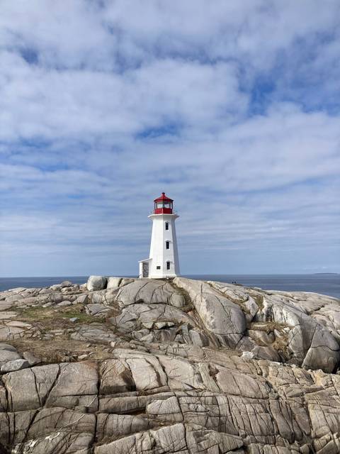 White and red lighthouse on rocky shore with ocean backdrop.