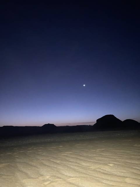 Night sky with moon over desert landscape.