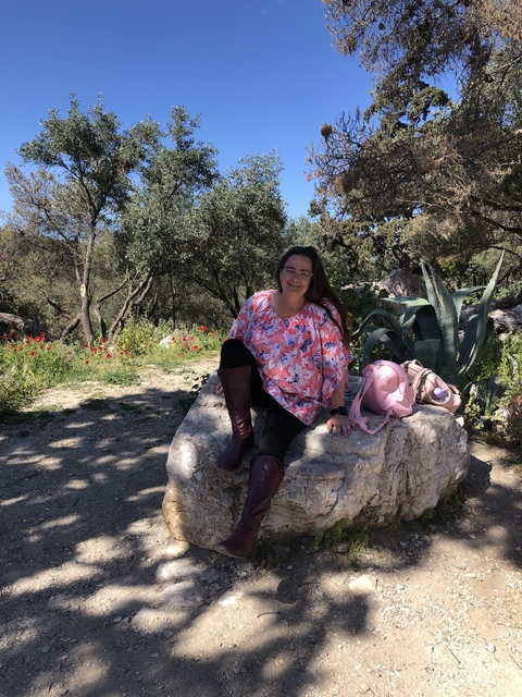 Woman sitting on a rock amidst greenery and flowers.