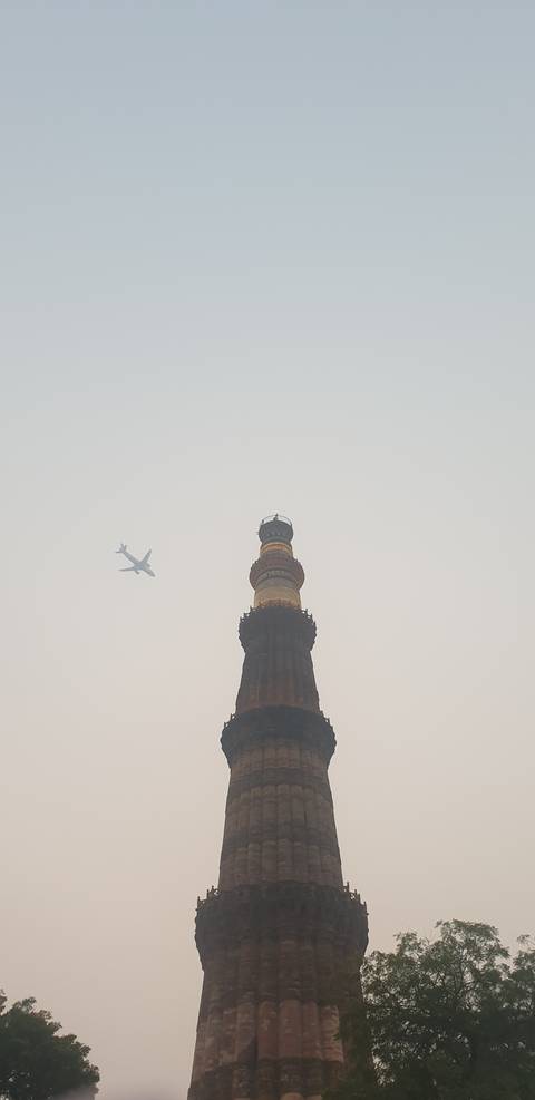 A tall historical tower with an airplane flying overhead.