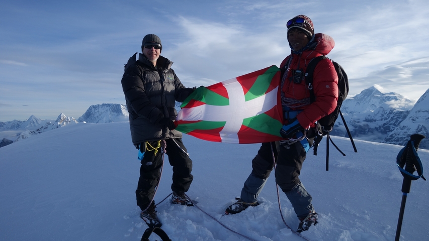 Two climbers with a flag standing on snowy peak.