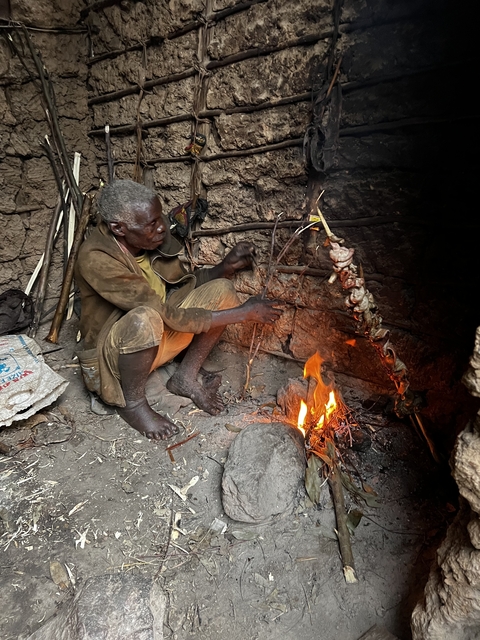       Person cooking meat over an open flame inside a rustic setting.
  